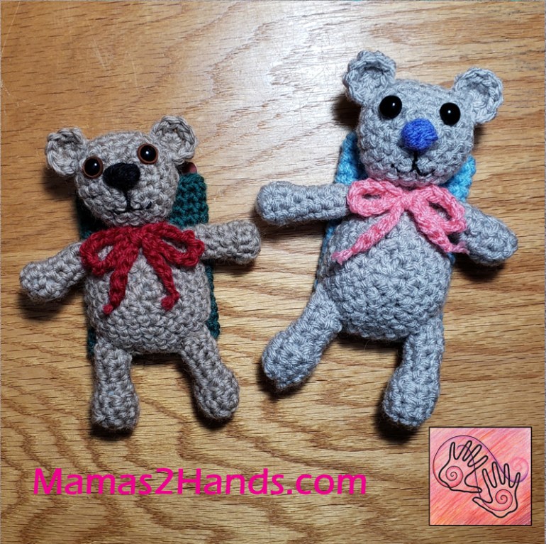 2 versions of "Beary Christmas Giftcard Holder". 1 bear is brown with brown eyes, black nose and red bow with a green pouch, other bear is gray with black button eyes, blue nose, pink bow and light blue pouch. Both are laying on a wooden background with Mamas2hands.com and logo at bottom of image.